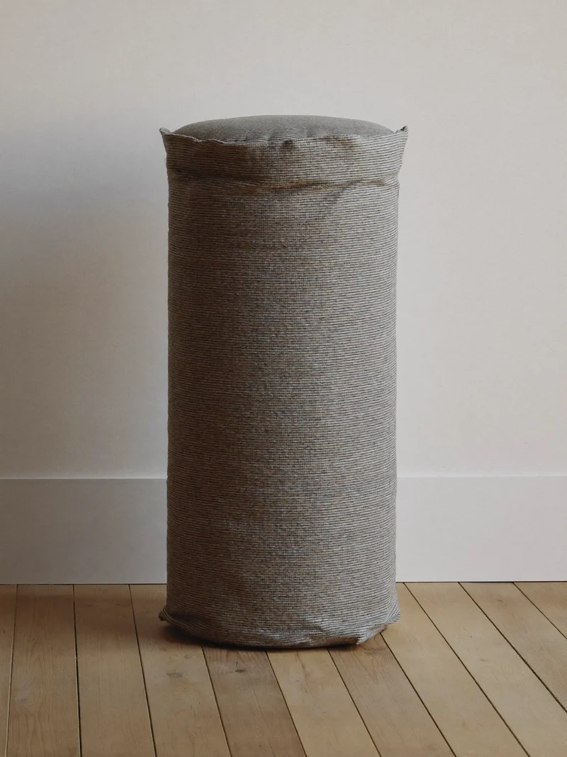 Traversin en coton tissé appuyé contre un mur de plâtre blanc